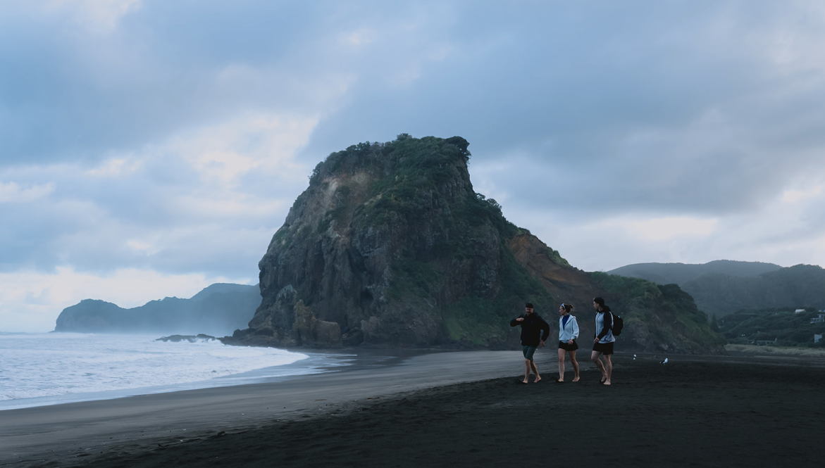 Tre utøvere går langs Piha-stranden i New Zealand